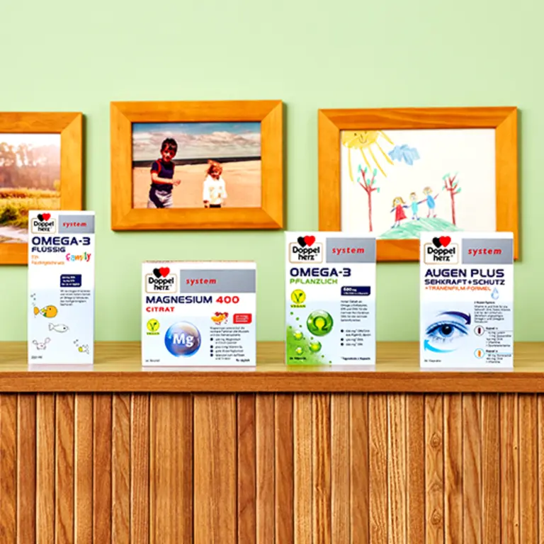 Image montrant une étagère en bois avec quatre boîtes de produits de santé. Les produits incluent Omega-3, Magnésium 400 Citrate et Augen Plus. En arrière-plan, il y a des photos et un dessin d'enfants sur un mur vert.